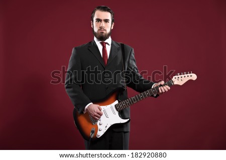 Retro fashion music man with beard wearing grey suit and red tie. Playing electric guitar. Studio shot.