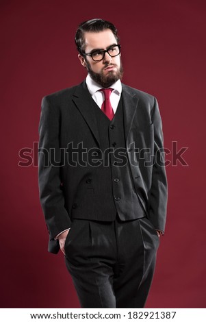Retro 1900 fashion man with beard wearing grey suit red tie and glasses. Studio shot.