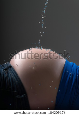 Pregnancy belly sprinkled with white and blue birth candies. Close-up.