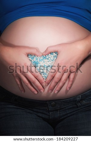 Pregnancy belly with hands and blue birth candies creating a heart shape. Close-up.