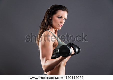 Fitness woman weight lifting with dumbbells. Wearing camouflage sportswear. Studio shot against grey.