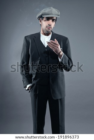 Mafia fashion man wearing grey striped suit with cap. Smoking cigarette. Black hair and brown skin. Studio shot.
