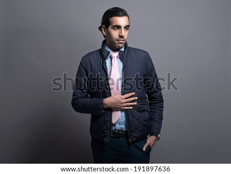 Contemporary fashion man wearing blue jacket and pink tie. Black hair and brown skin. Studio shot against grey.
