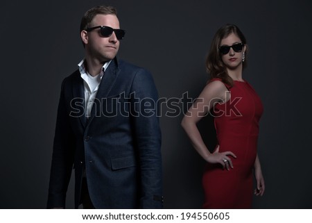 Fashion couple wearing a red dress, black sunglasses and blue jacket. Young man and woman. Studio shot against grey.