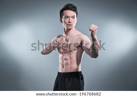 Muscled asian kung fu man in action pose. Blood stripes on his chest. Wearing black pants. Studio shot against grey.