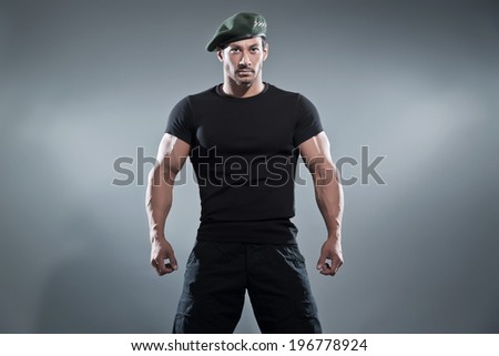Commander muscled action hero man wearing black t-shirt and pants. Studio shot against grey.