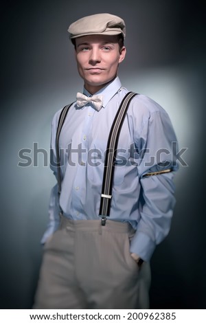 Retro classic dandy fashion man wearing cap with blue shirt braces and bow tie. Studio shot.
