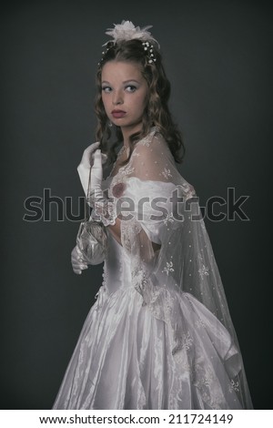 Victorian fashion woman wearing white dress. Holding handbag. Studio shot against grey.