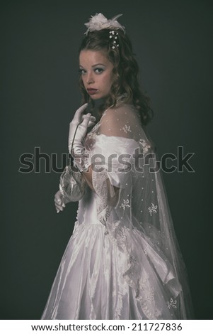 Victorian fashion woman wearing white dress. Holding handbag. Studio shot against grey.