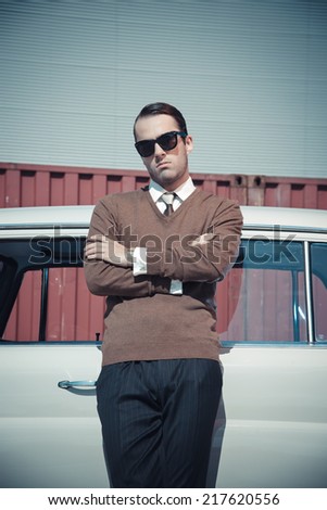 Retro fifties business fashion man with sunglasses leaning against vintage car.