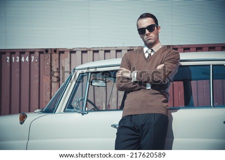 Retro fifties business fashion man with sunglasses leaning against vintage car.