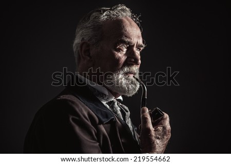 Pipe smoking vintage characteristic senior man with gray hair and beard. Studio shot against dark background.