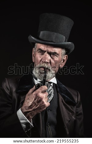 Pipe smoking vintage victorian man with black hat and gray hair and beard. Studio shot against dark background.