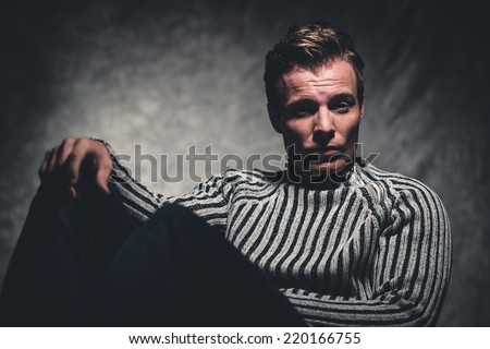 Retro fifties cool rebellion fashion man wearing striped woolen sweater. Gray wall.