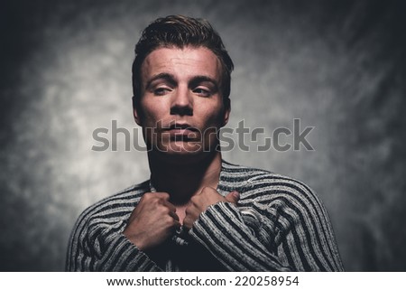 Retro fifties cool rebellion fashion man wearing striped woolen sweater. Gray wall.