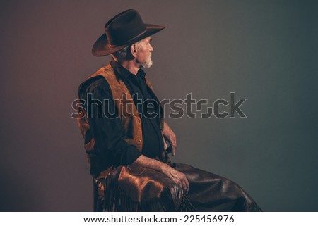 Old rough western cowboy with gray beard and brown hat. Low key studio shot.