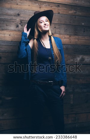 Cowgirl jeans fashion woman with long blonde hair. Standing against wooden wall.