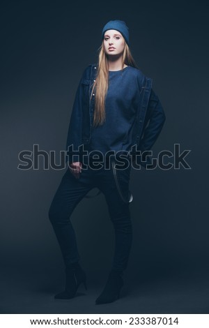 Woman jeans winter fashion wearing blue cap. Long blonde hair. Studio shot against grey.