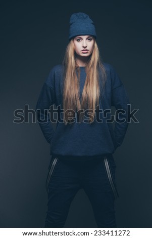 Woman jeans winter fashion wearing blue cap. Long blonde hair. Studio shot against grey.