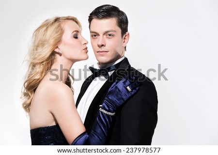 Romantic new year\'s eve fashion couple. Woman kissing man. Wearing black dinner jacket and blue dress. Isolated against white.