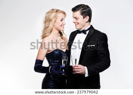 Romantic new year\'s eve fashion couple toasting with champagne. Wearing black dinner jacket and blue dress. Isolated against white.