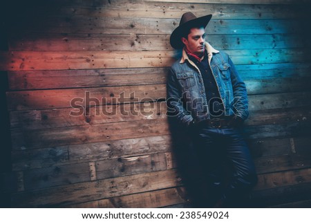 Winter cowboy jeans fashion man. Wearing brown hat, jeans jacket and trousers. Leaning against old wooden wall.