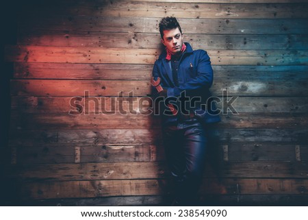 Winter jeans workwear fashion man with short dark hair. Holding old big spanner. Leaning against old wooden wall.