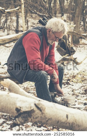 Sitting Old Man at the Forest Cooking for Food Using his Small Portable Stove