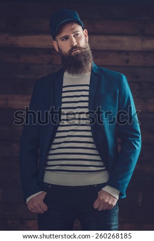 Portrait of a Stylish Young Good Looking Goatee Guy in Fashionable Attire Looking to the Right of the Frame on a Wooden Wall Background.