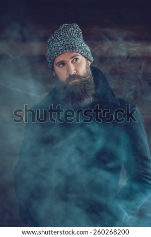 Handsome Man with Long Beard, Wearing Casual Winter Outfit Behind a Smoke, Looking Afar.