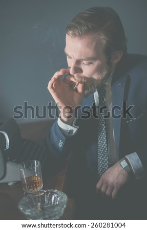 Businessman sitting smoking and drinking alcohol at his desk in the office getting ready to stub out a cigarette in an ashtray