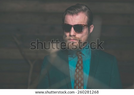 Close up Middle Age Man with Beard and Mustache Wearing Elegant Formal Fashion with Sunglasses on Wooden Wall Background.