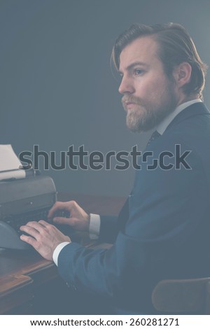 Retro businessman, journalist or writer sitting at an old-fashioned manual typewriter looking thoughtfully off to the side