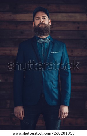 Portrait of a Handsome Goatee Man, Wearing Dark Blue Formal Wear with a Cap, Looking at the Camera on a Wooden Wall.