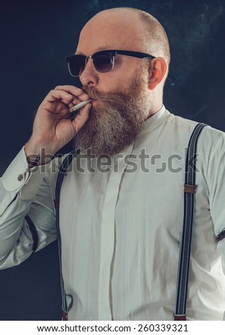 Close up Middle Age Bald Goatee Man, in White Long Sleeves Shirt with Suspenders and Eye Wear, Smoking a Cigarette on a Gray Background.