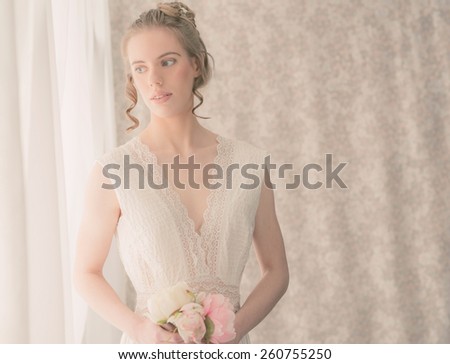 Close up Half Body Shot of an Elegant Young Woman in White Lace Dress, Holding Fresh Rose Flowers, Standing Beside the Window with Curtains While Looking Outside.