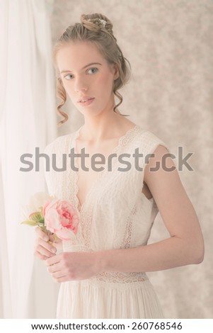 Portrait of a Pretty Young Woman in White Elegant Dress Holding Fresh Pink Rose Flowers While Looking to the Right of the Frame.
