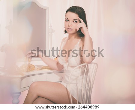 Close up Sitting Pretty Woman in Sexy White Nightie Looking to the Right with Hand on her Face While Sitting on a Chair In Front of a Mirror.