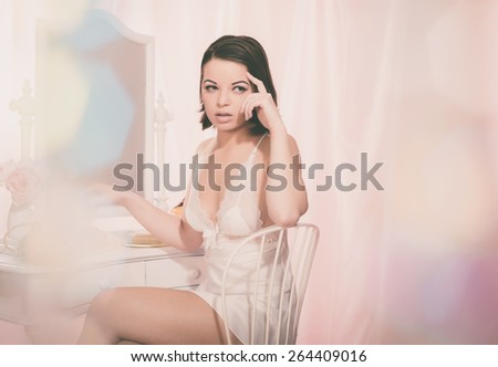 Sexy Young Woman Wearing White Nightie Sitting on a Chair and Looking to the Right Seriously Behind a Glittery Sequins Curtain