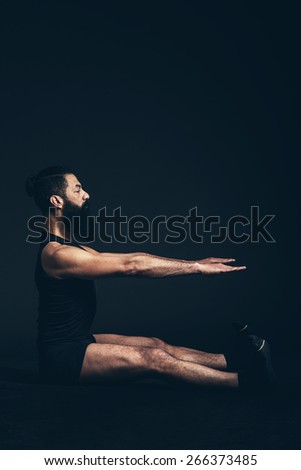 Athletic Young Man with Goatee Beard Sitting on the Floor with Both Arms and Legs Stretched Forward, Isolated on Black Background.