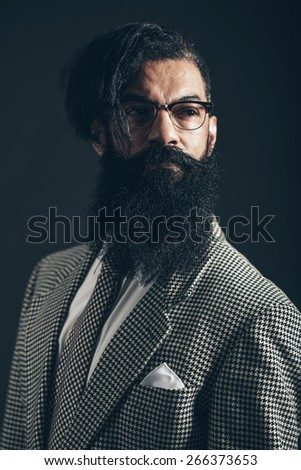 Close up Serious Man with Long Beard and Mustache, Wearing Formal Checkered Suit, Looking to the Right of the Frame on a Black Background.