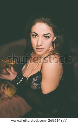 Close up Elegant Young Woman Wearing Black Lingerie Holding a Bottle of Perfume While Looking at the Camera Seductively. Captured Indoor on a Black Background.