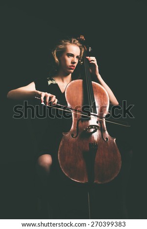 Attractive young woman playing the cello in the darkness at a recital or classical concert, full length portrait