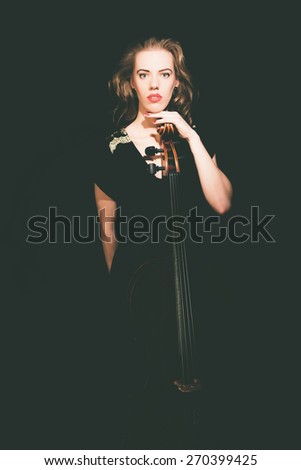 Portrait of a Serious Woman Cellist Standing and Leaning on Cello Instrument and Staring at Camera on a Black Background.