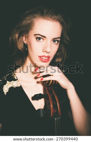 Classical beauty playing a classical instrument with a gorgeous young cellist holding her cello as she looks at the camera with a quiet smile, close up of her face