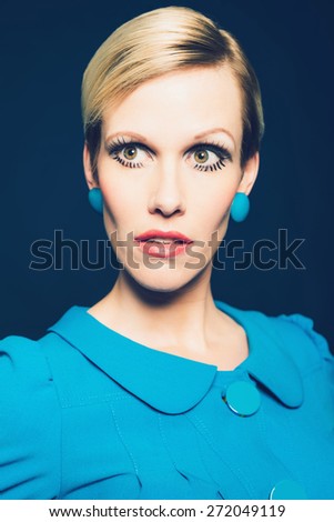Serious mature blond woman with an elfin face and serious expression wearing a stylish blue dress and earrings
