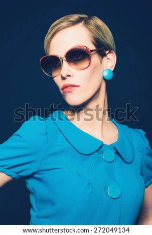 Close up Portrait of a Stylish Young Woman Wearing Plain Blue Dress and Earrings with Sunglasses, Looking to the Left, Isolated on Dark Blue.