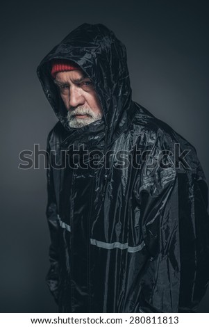 Portrait of a Freezing Bearded Senior Man, Wearing Black Waterproof Jacket, Looking at the Camera. Captured in Studio with Black Background.