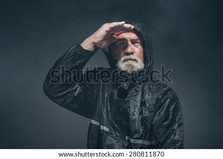 Portrait of a Bearded Middle Age Man with Facial Hair, Wearing Black Rain Jacket, Looking Afar with a Serious Facial Expression.