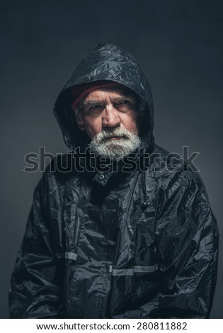 Close up Serious Adult Guy with Beard and Mustache, Wearing Black Rain Jacket, Looking at the Distance While Thinking of Something. Captured in Studio with Black Background.